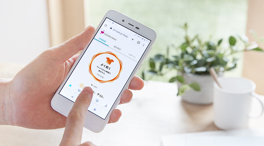 ココロウォッシュアプリ起動中のスマートフォンを手に、サービスを利用しているイメージ図。
